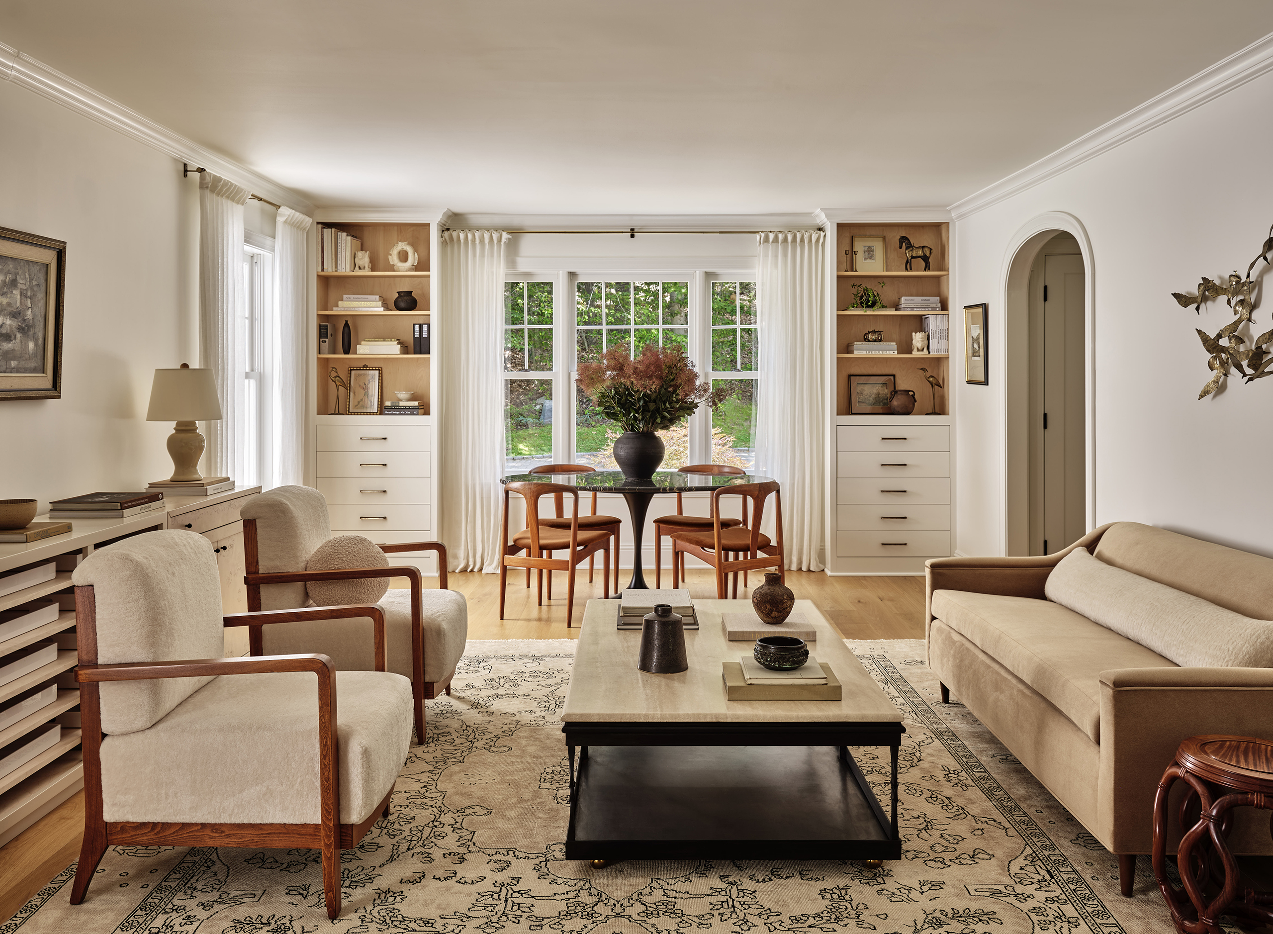 A serene and elegantly styled living room bathed in natural light, featuring mid-century modern furniture, built-in shelving, and a harmonious blend of warm neutrals and natural textures.