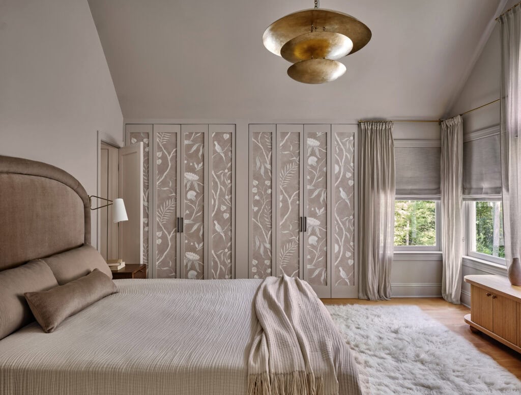 A serene and sophisticated bedroom featuring soft neutral tones, elegant floral-paneled wardrobes, and layered textures for a cozy yet refined ambiance. The statement lighting and plush rug add warmth and depth to this tranquil retreat.